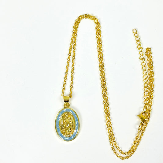 Gold chain necklace with an oval pendant featuring a gold religious medallion over a light blue patterned background, displayed on a plain white surface.