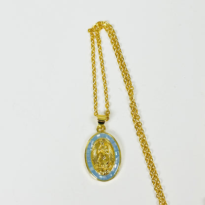 Gold chain necklace with an oval pendant featuring a gold religious medallion over a light blue patterned background, displayed on a plain white surface.