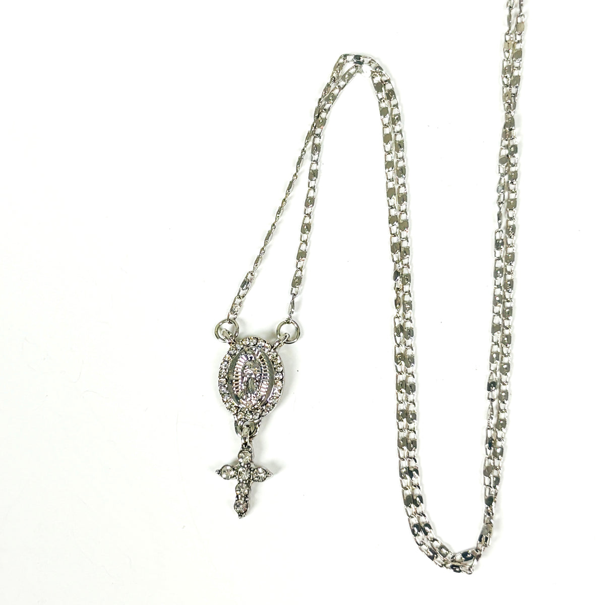 Silver-tone chain necklace with an oval religious pendant and dangling cross, set with clear rhinestones on a white background.