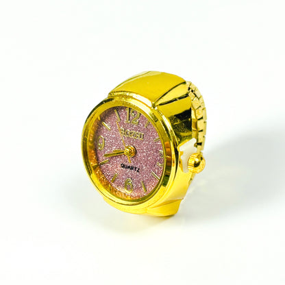 A gold-colored ring-shaped quartz watch with a glittery pink face and gold-tone hands and numerals, set against a plain white background.