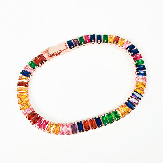 A rose gold tennis bracelet featuring a continuous row of colorful rectangular baguette gemstones in shades of pink, orange, yellow, green, blue, and purple, displayed on a clean white background.