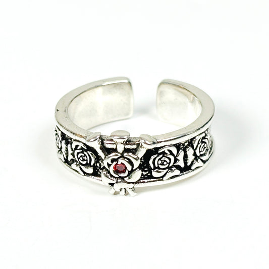 An antique silver-tone open band ring featuring an embossed floral pattern and a small red gemstone at the center, shown on a plain white background.